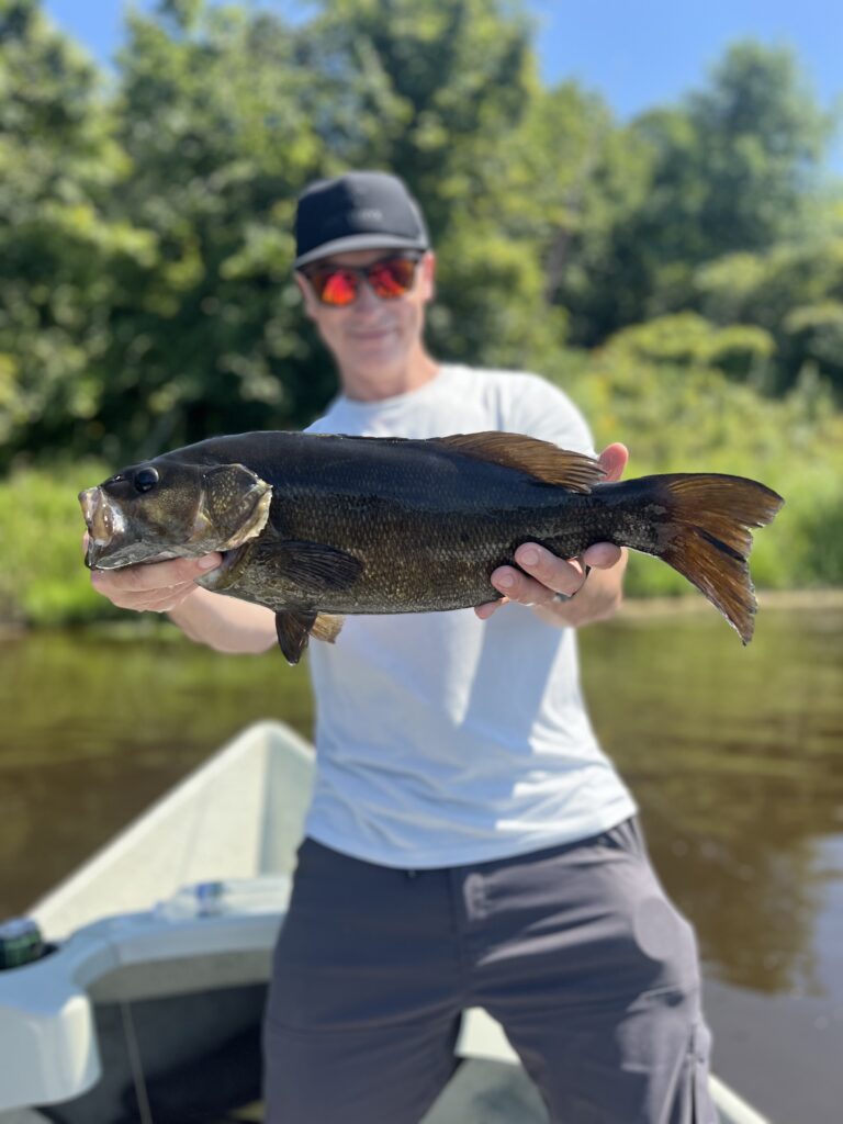 A fisherman displays a dark, healthy Smallmouth Bass caught on a fly, showcasing the premier smallmouth guiding of The Ridge Fly Fishing.